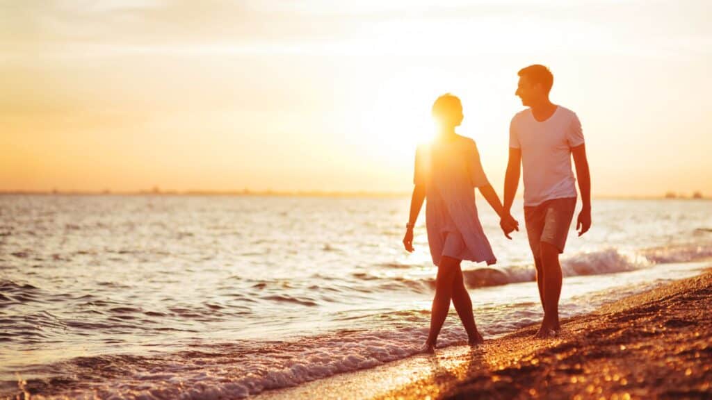 happy couple walking down the beach at sunset